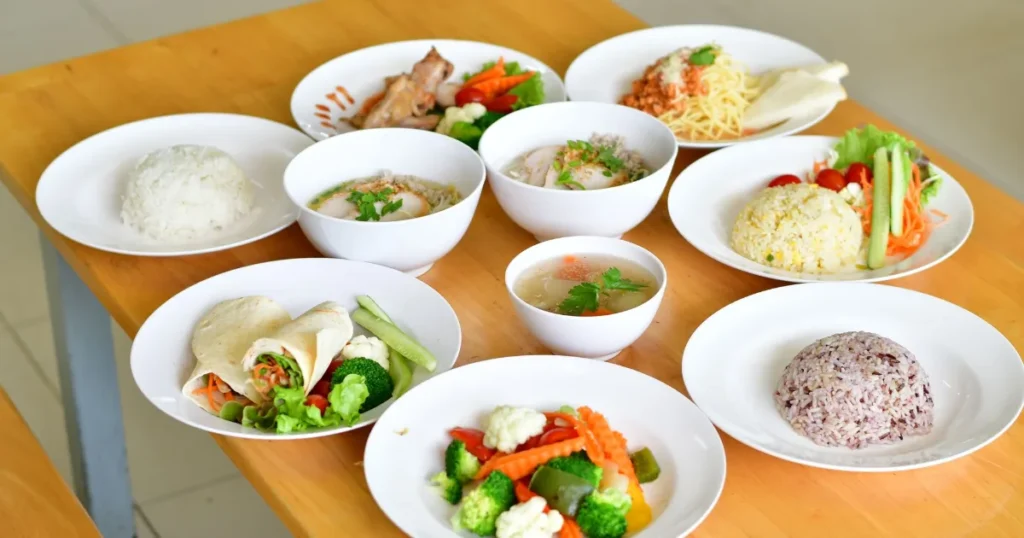 Mesa de madeira com pratos variados de comida caseira, incluindo arroz, sopa e legumes
