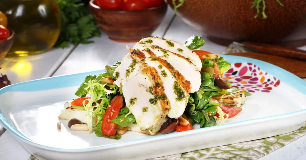 Prato com peito de frango grelhado fatiado sobre folhas verdes e tomate