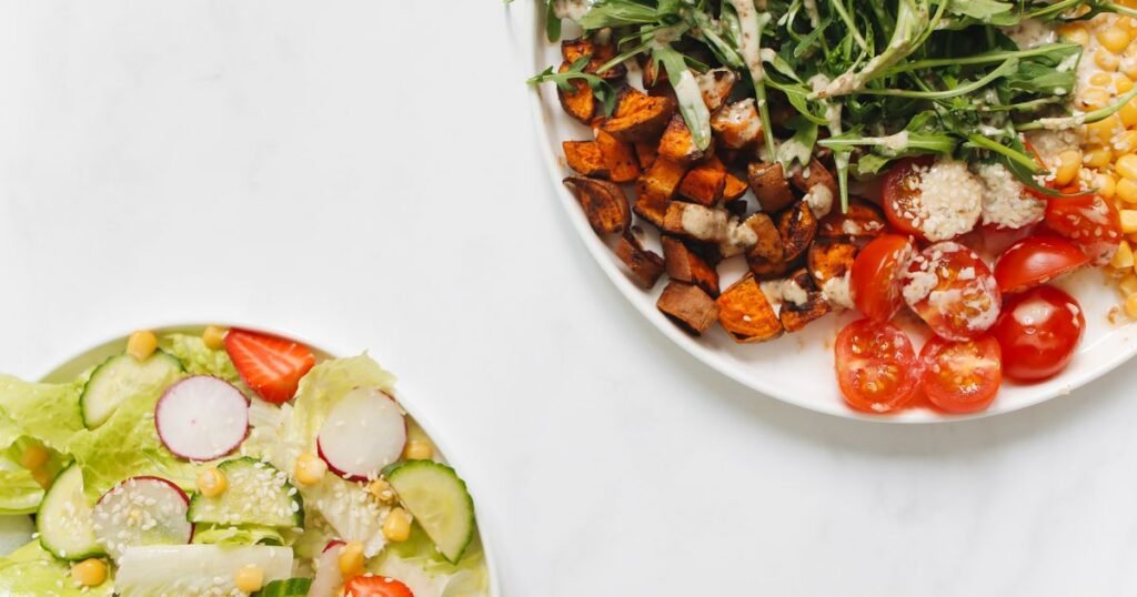 Dois pratos de comida saudável com legumes, batata-doce, tomate e folhas verdes
