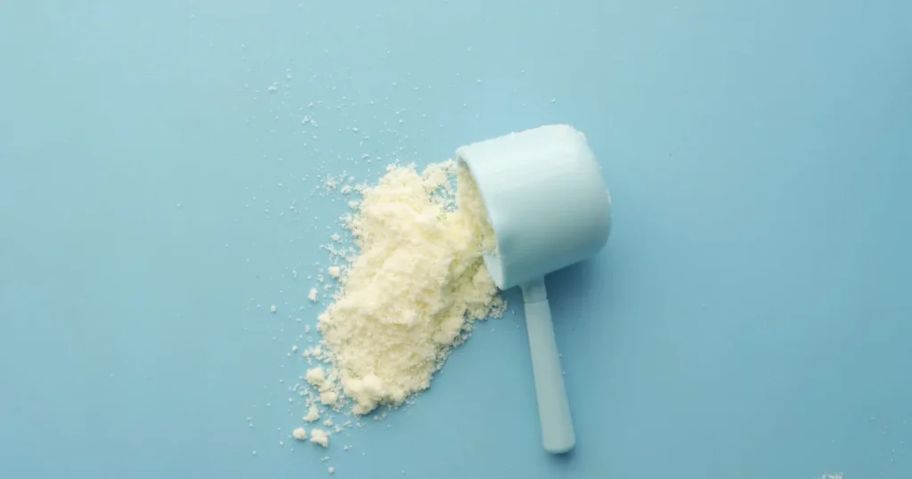 Pó branco de creatina derramando de um dosador sobre fundo azul