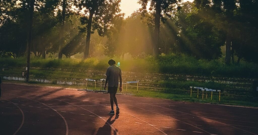Corredor visto de costas correndo numa pista ao nascer do sol, com raios de luz entre as árvores