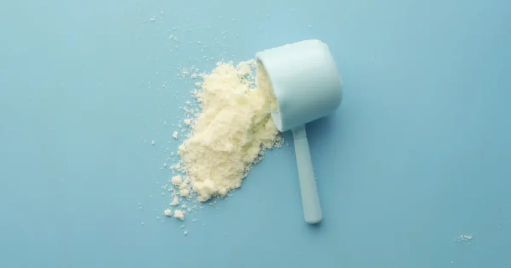 Dosador com pó de creatina derramado sobre superfície azul
