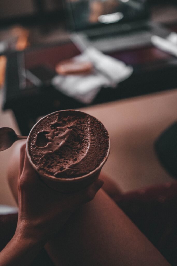 Mão segurando um pote de sorvete de chocolate, gesto associado a comer por vontade emocional